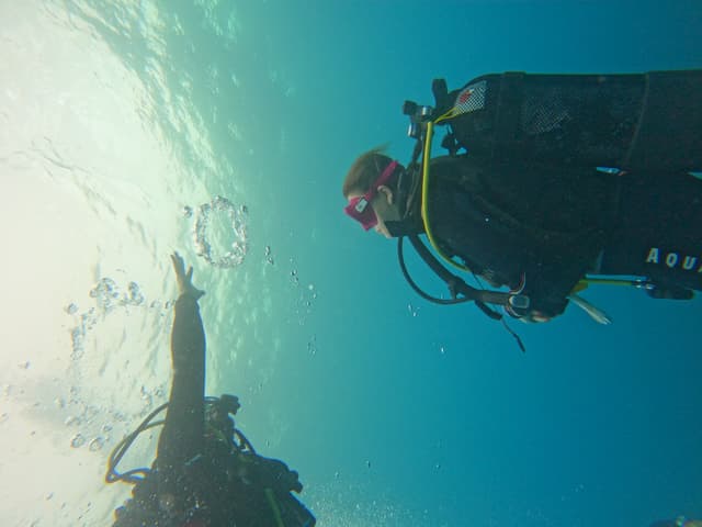 Deux plongeurs remontant vers la surface en fin de plongée, silhouettes à contre-jour dans l'eau bleue